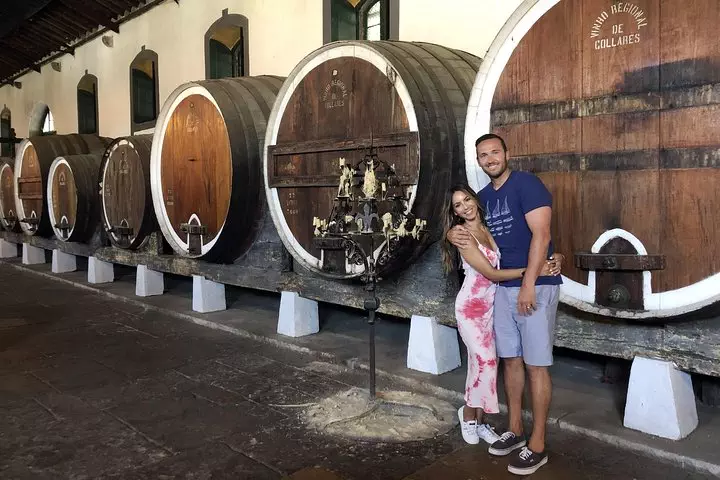 Couple visiting Adega Regional de Colares during a private wine tasting tour in Sintra, Portugal, surrounded by traditional oak wine barrels.