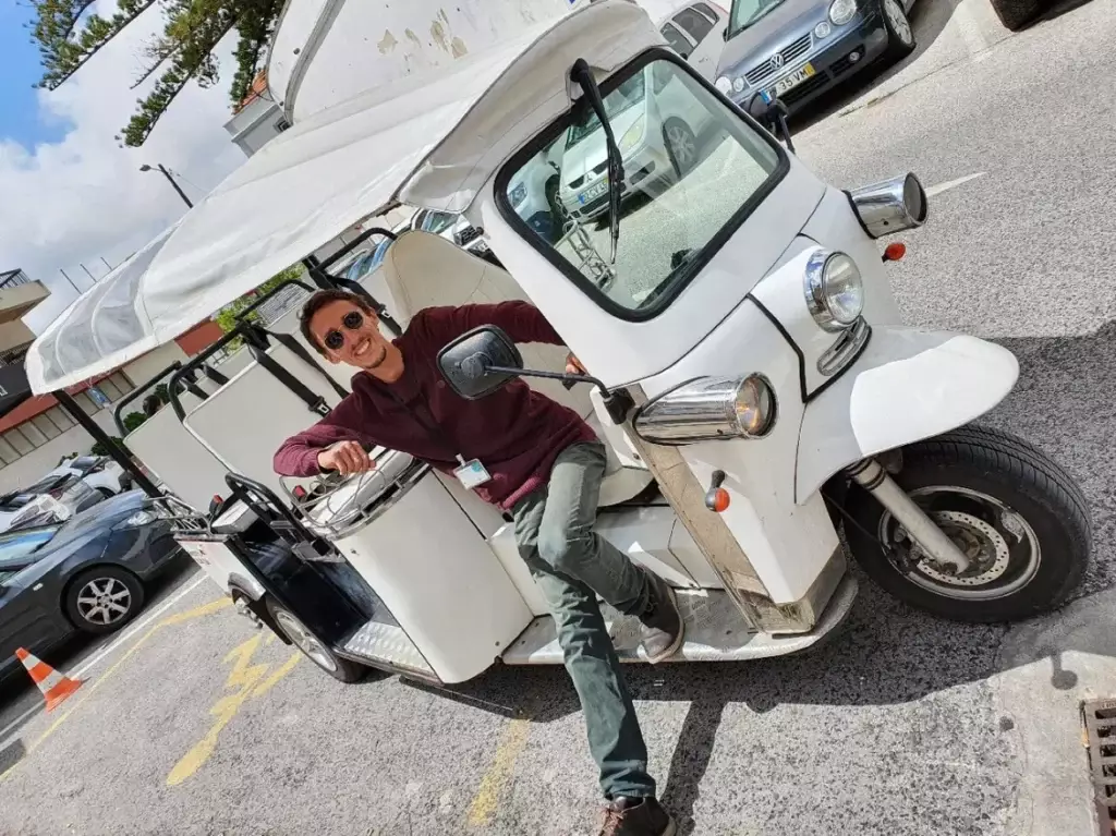 Daniel Ponce, smiling and wearing sunglasses, poses confidently in the driver’s seat of a white electric tuk-tuk during a Yes, You Deserve tour in Sintra, ready to lead another unforgettable adventure.