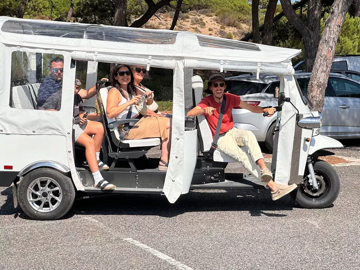 Daniel Ponce drives a white electric tuk-tuk filled with smiling tourists during a sunny Yes, You Deserve tour in Sintra. The group looks excited and ready to explore, enjoying a fun and eco-friendly ride through scenic landscapes.