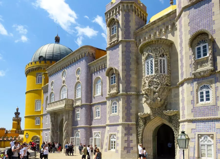 Front view of the stunning tiled façade and domed tower of Pena Palace in Sintra, Portugal, with tourists exploring its Romantic architecture — a highlight of Yes, You Deserve’s private tuk tuk tours in Sintra.