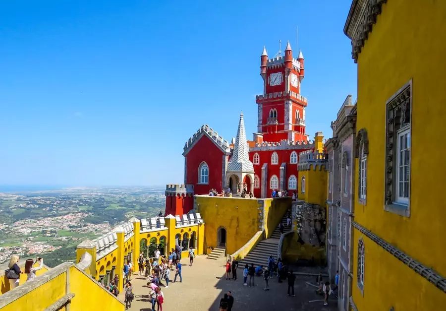 Colorful courtyard and panoramic view from Pena Palace in Sintra, Portugal, with tourists exploring the red, yellow and tiled sections of the romantic palace — part of a guided Yes, You Deserve tuk tuk experience.