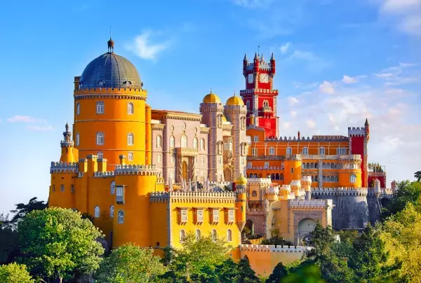 Vibrant Pena Palace in Sintra, Portugal, with its iconic yellow and red towers bathed in sunlight against a clear blue sky and lush green surroundings.