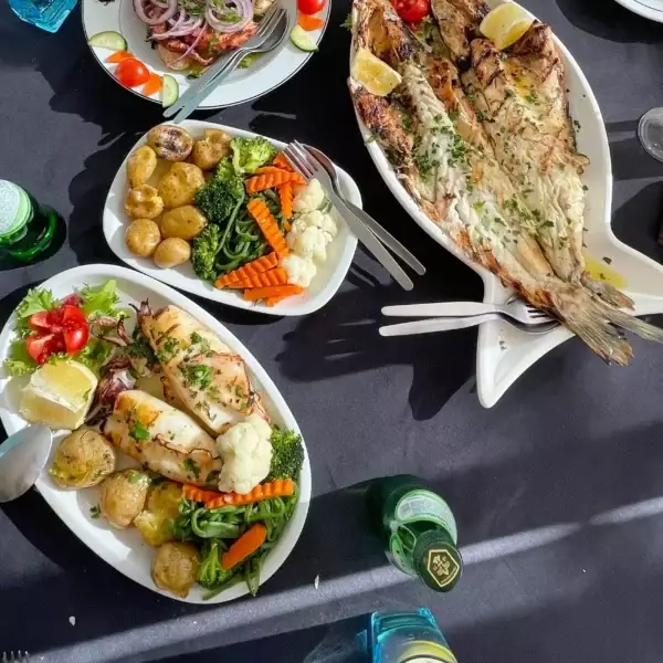 A colorful and fresh Portuguese seafood meal served on a black tablecloth, featuring grilled fish, squid, boiled potatoes, mixed vegetables, and a salad. Captured during a Yes, You Deserve tour lunch stop in Sintra.