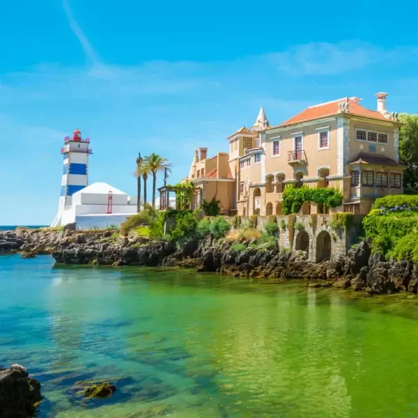 Scenic view of Santa Marta Lighthouse and museum in Cascais, Portugal, with turquoise waters, palm trees, and traditional Portuguese architecture – perfect stop on a Cascais day tour.