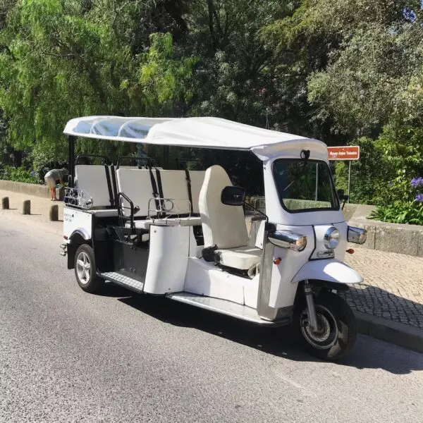 A white electric tuk-tuk parked on a quiet road in Sintra, Portugal, ready to take guests on a scenic and eco-friendly adventure with Yes, You Deserve. Surrounded by lush greenery and cobblestone paths, it offers a charming and sustainable way to explore the town.