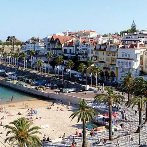 Aerial view of Cascais beach and historic town center with palm trees, colorful buildings, and people enjoying the sun – popular seaside destination near Lisbon.