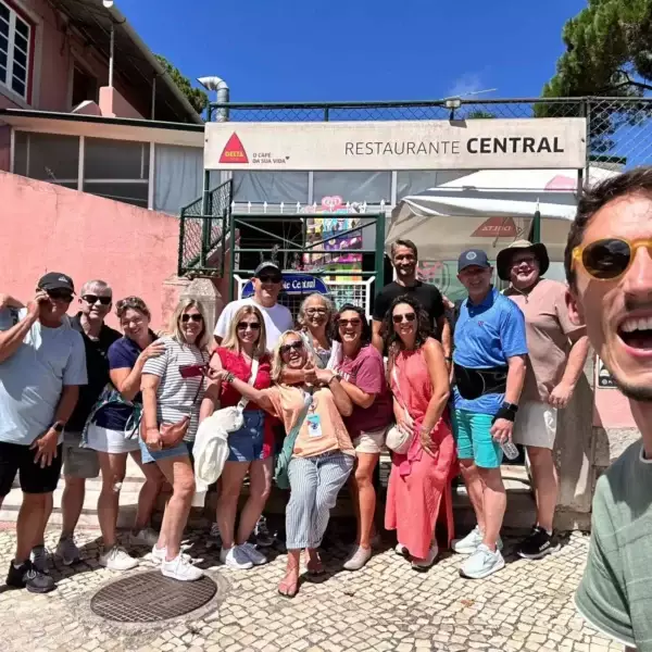 A cheerful group of tourists and their smiling guide pose in front of Restaurante Central in Sintra, Portugal, during a tour with Yes, You Deserve. The sunny day and relaxed atmosphere highlight the joy of the experience.