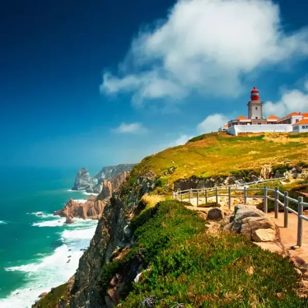 Scenic view of Cabo da Roca, the westernmost point of continental Europe, featuring dramatic cliffs, the Atlantic Ocean, and a historic lighthouse under a vibrant blue sky. A popular stop on the Yes, You Deserve Sintra and coastal tour.